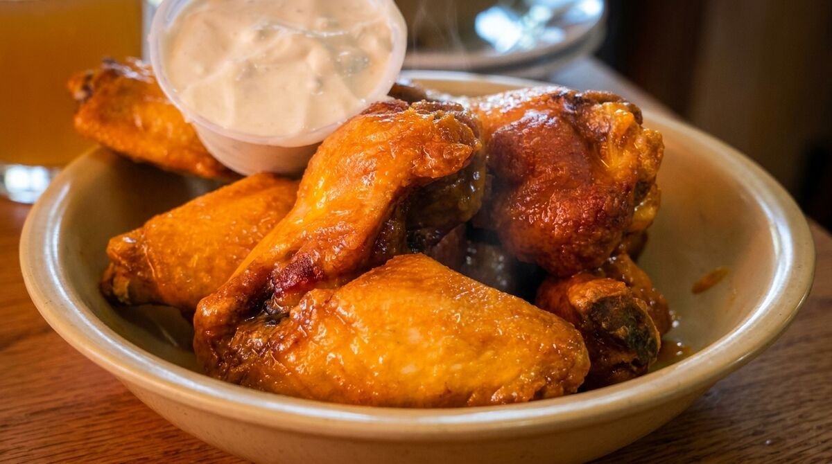 A bowl of golden-brown chicken wings with a side of ranch dressing, steam rising from the wings.